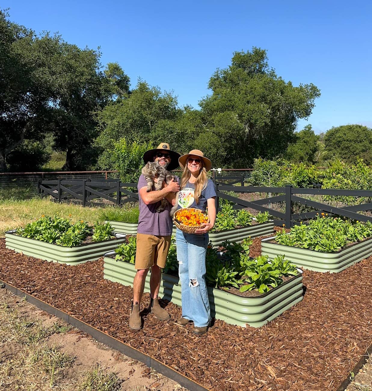 Aaron and DeannaCat stand in front of their new calendula garden space where metal raised beds are full of calendula plants. 