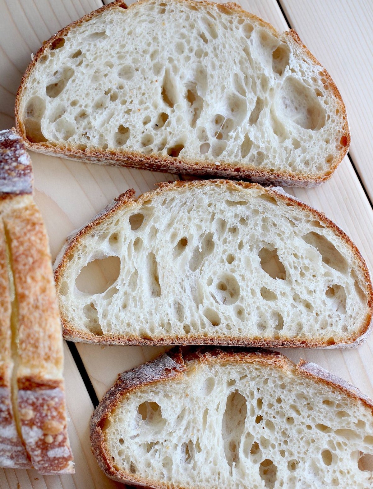 Fresh slices of bread are laid out flat next to a loaf of bread. 