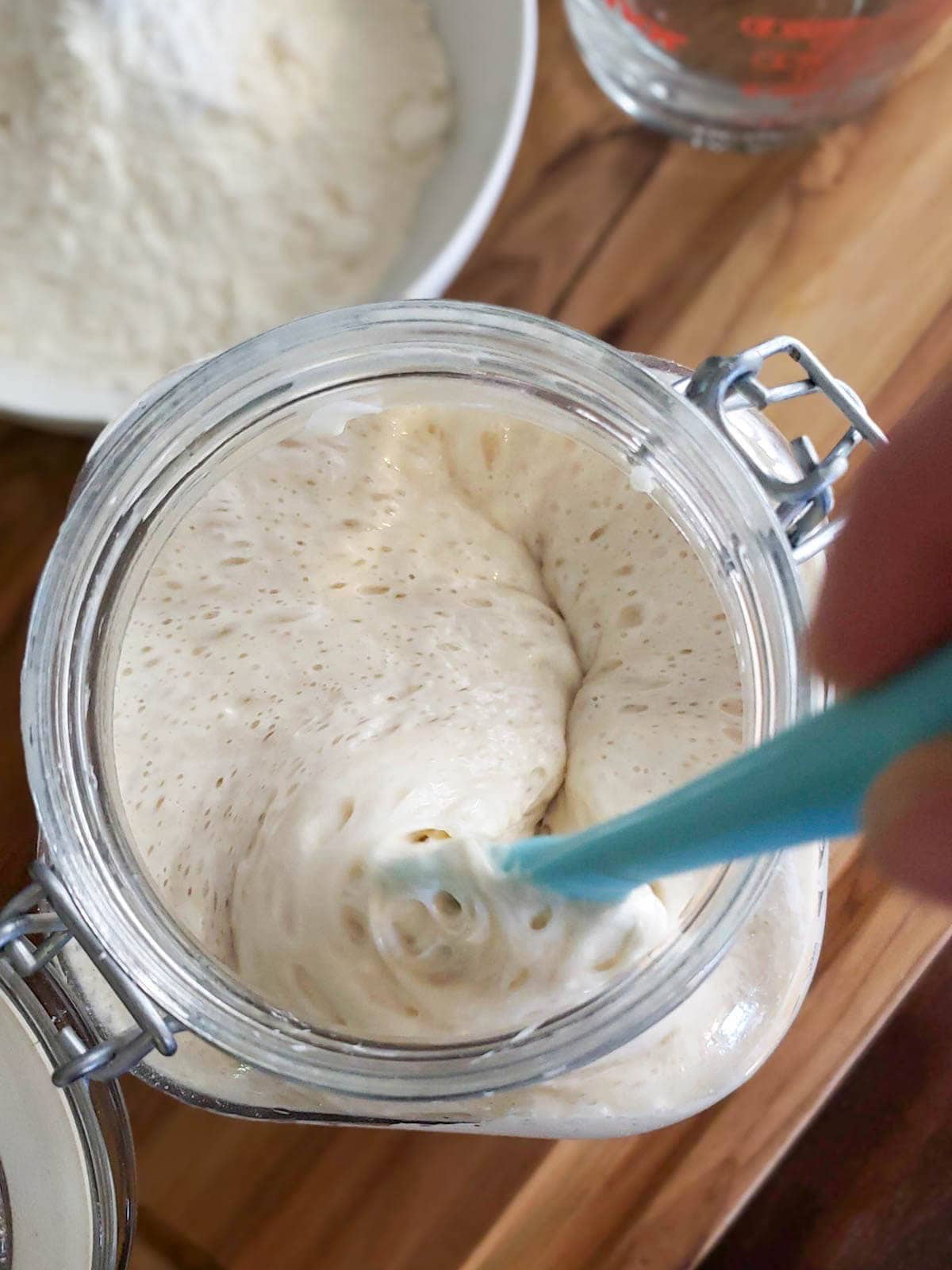 The silicone spatula is stirring a mixture inside of tall glass container. 