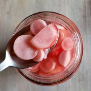 A spoon full of pink fermented homegrown radish slices