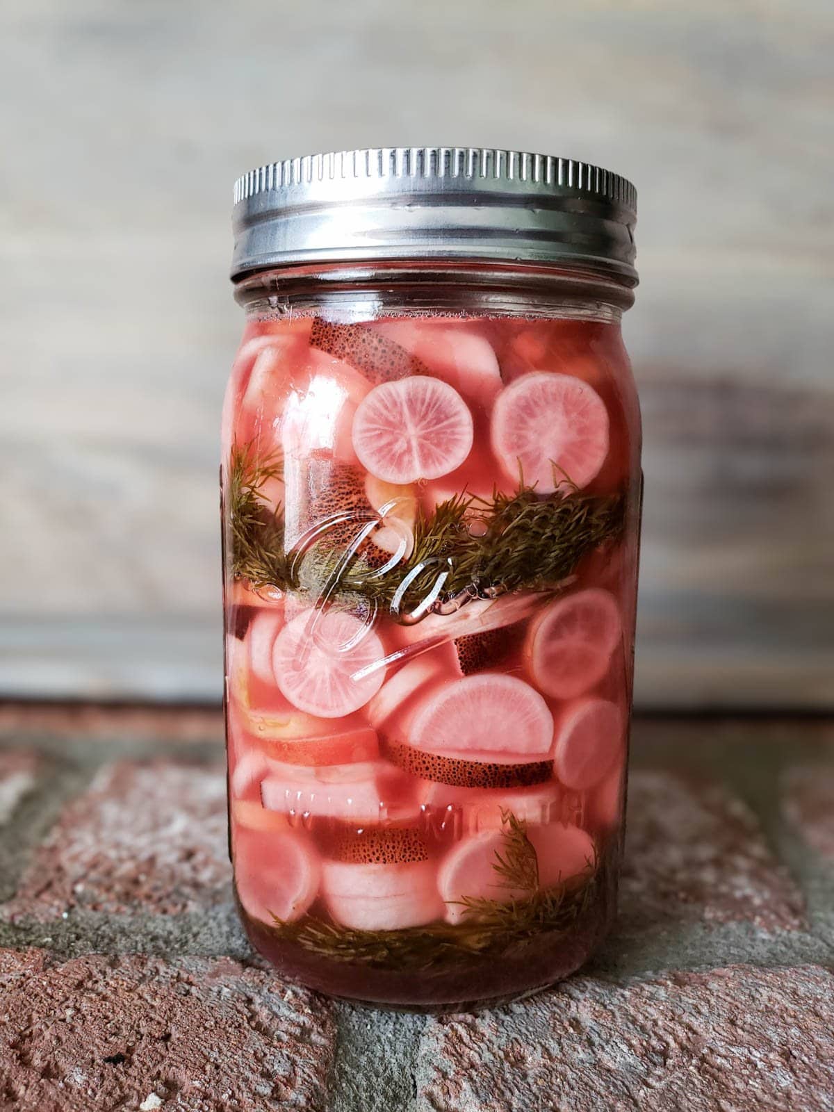 One week later, the jar of fermented radishes has turned bright pink (including the brine) and the dill has faded to olive green. The airlock lid has been replaced with a standard flat jar lid (stainless steel to prevent rust)