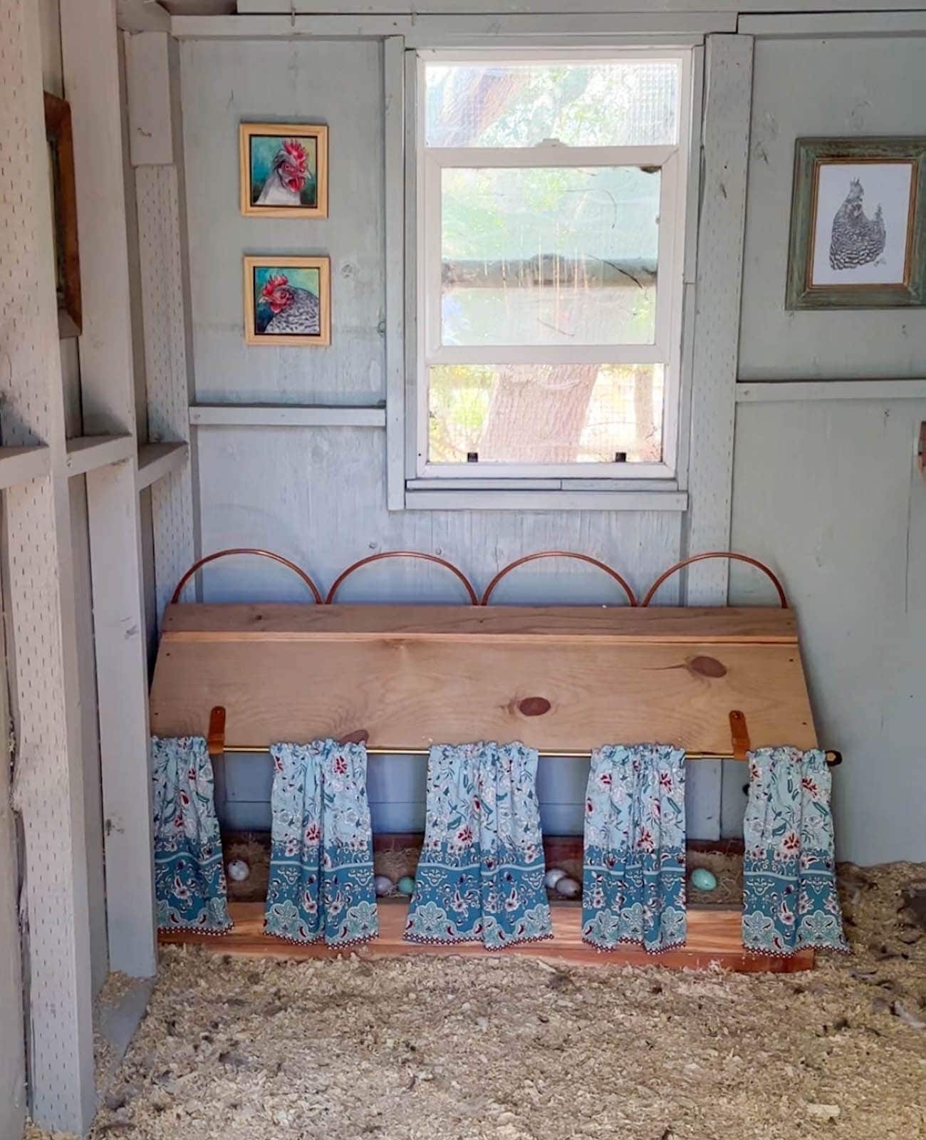 Four nest boxes sit along a coop wall, curtains are hung on the outside of each box while a few wood eggs are inside each box.