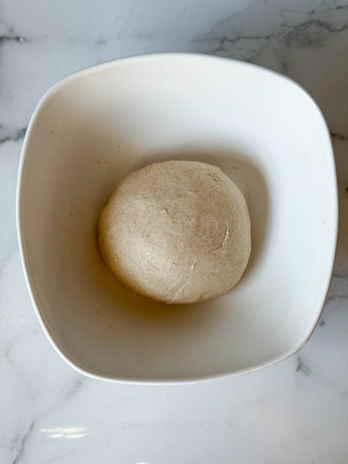 A dough ball sits inside of a large white ceramic bowl. 