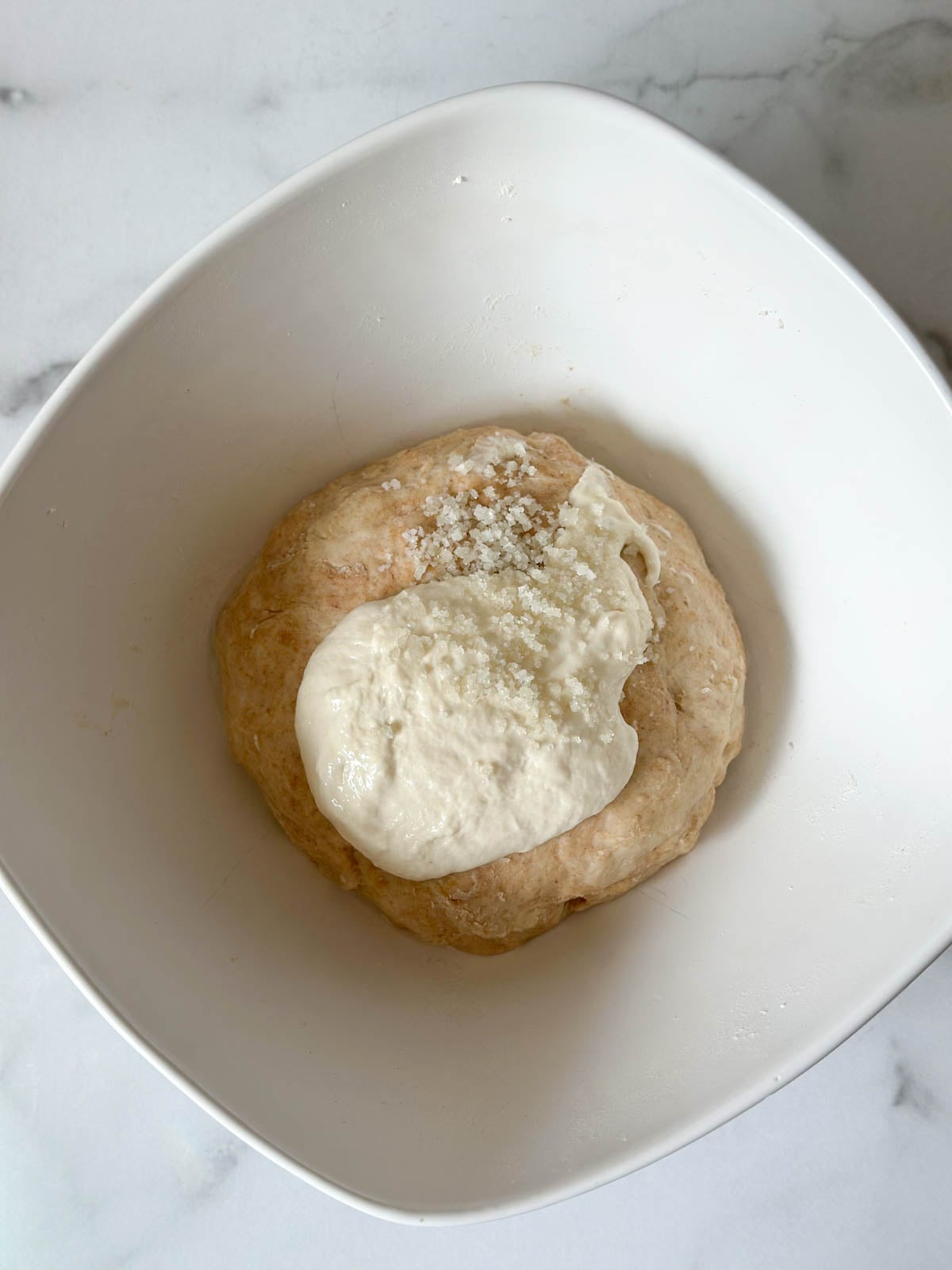 Sourdough starter and salt sit on top of a dough ball of flour and water. 