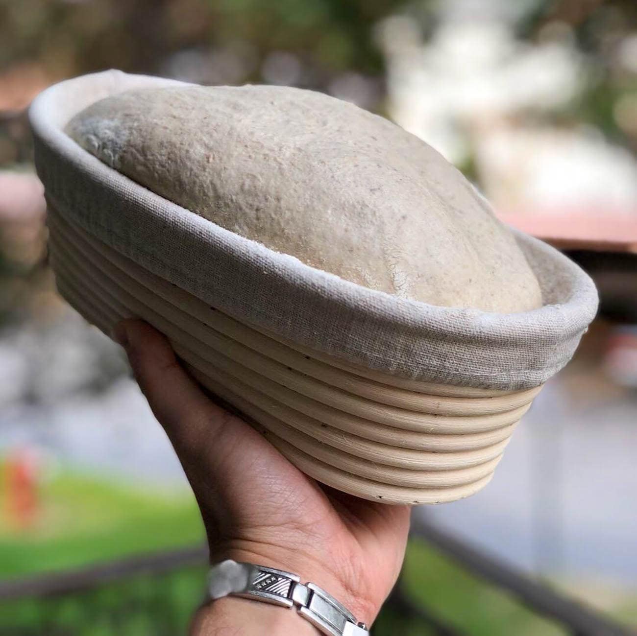 A hand holds a batard banneton which contains bread dough. 