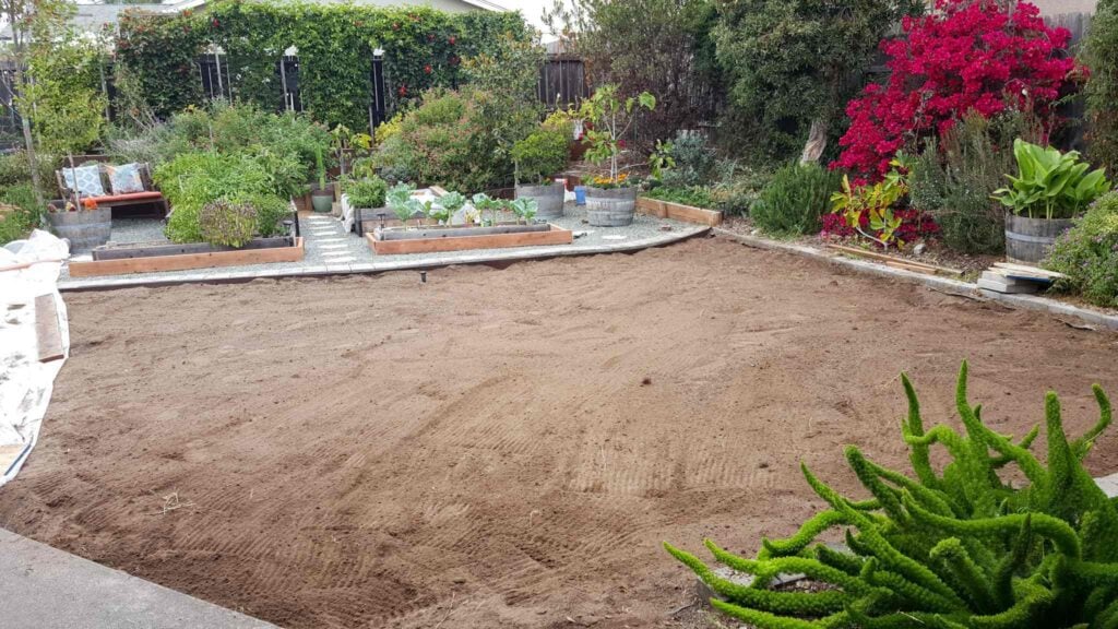 An open dirt yard with a garden space beyond set in gravel hardscape with flagstone pavers.