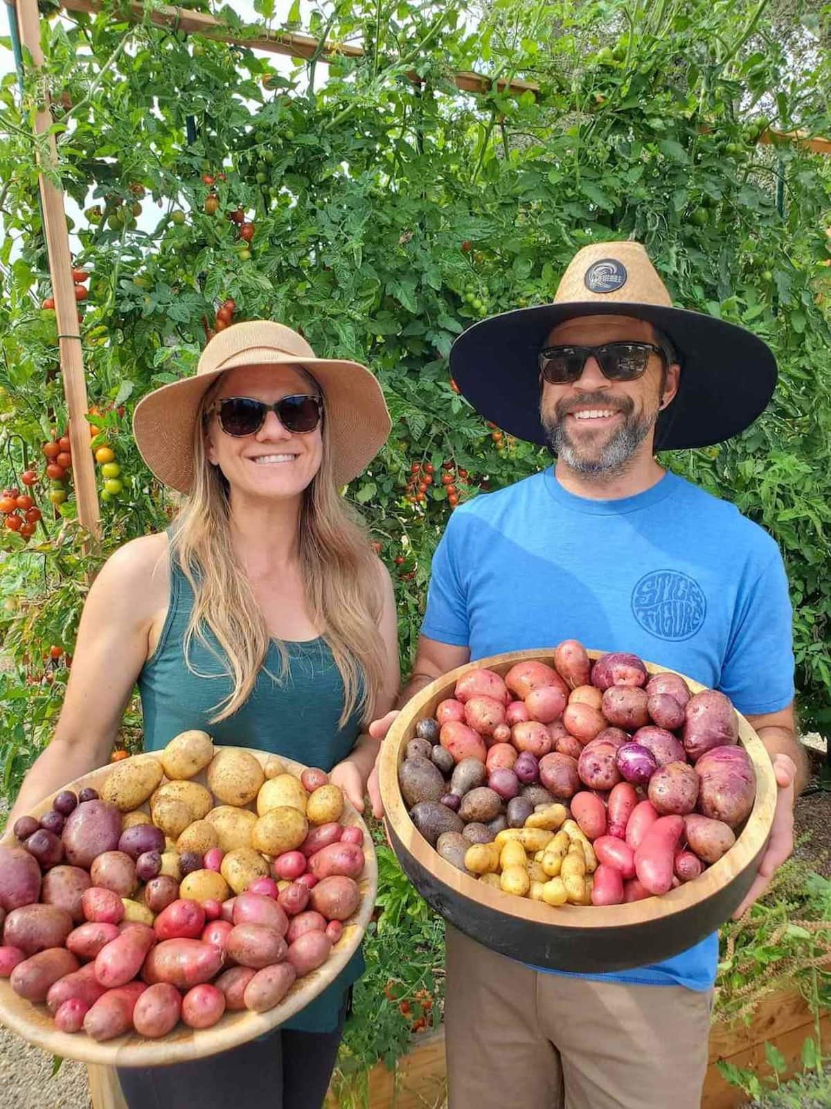 Aaron and Deanna are each holding a wooden bowl full of freshly harvest potatoes after growing them in containers.