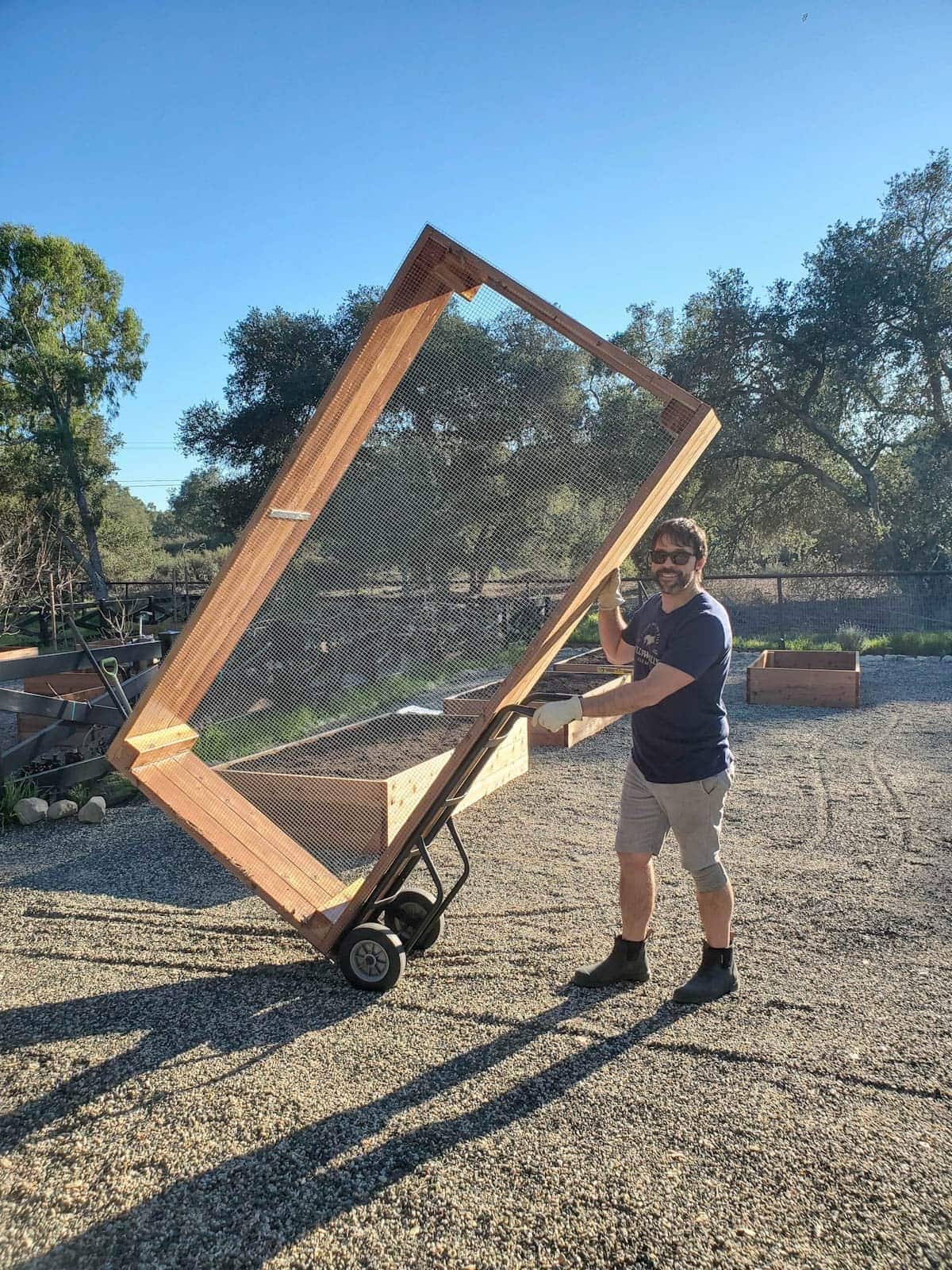A man has a finished raised garden bed on a dolly as it gets maneuvered into place.