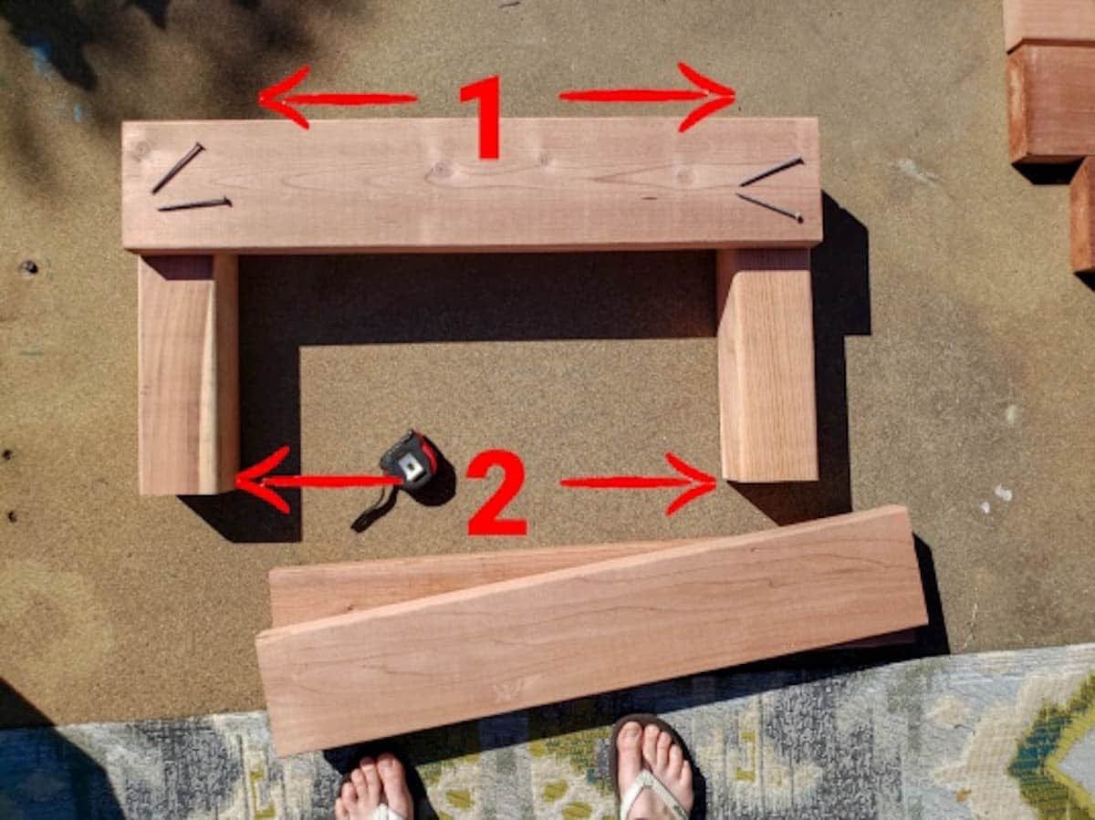 Two 4x4s lay on the ground, equal distances apart at each end. Then the 2x6" cut boards are being laid on top.