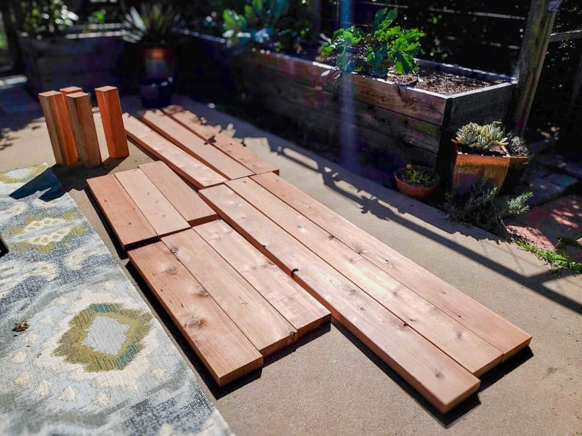 a dozen cut redwood boards laying on a concrete patio, waiting to be put together into a raised bed.