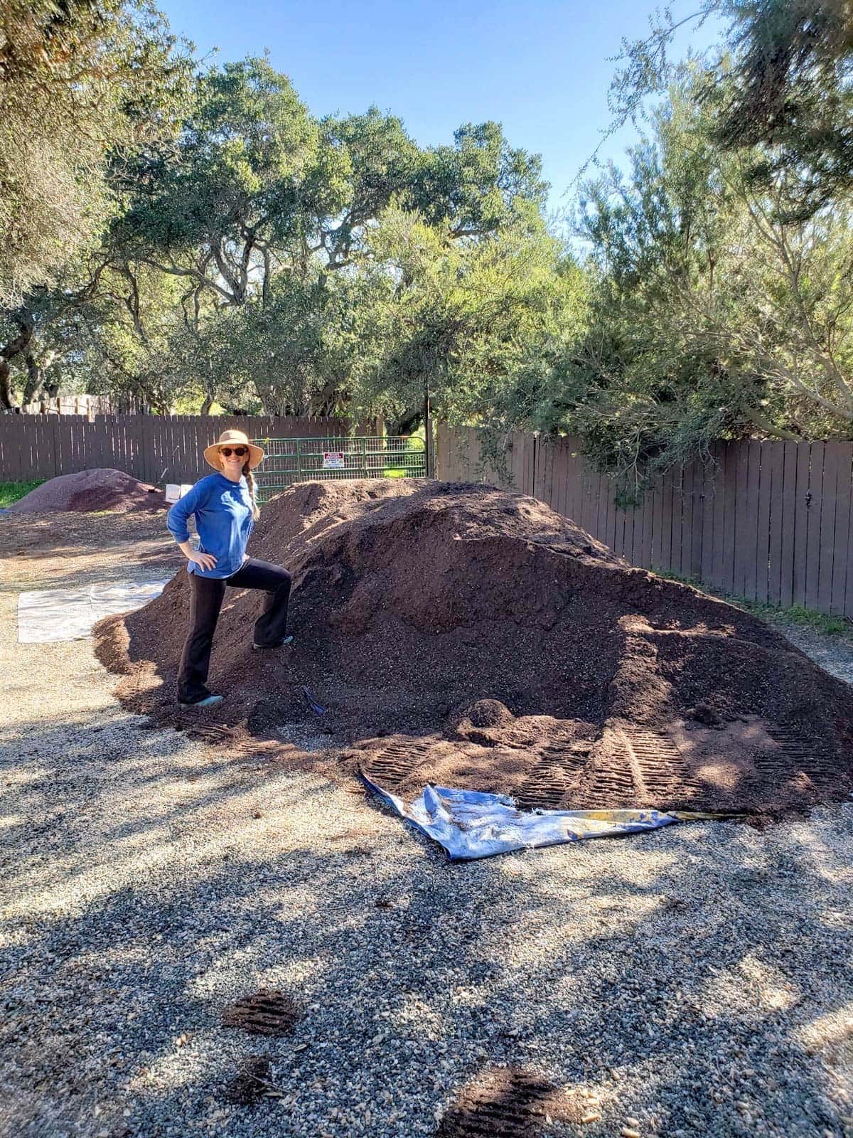 Deanna standing next to a huge pile of bulk performance blend soil. Beyond is a small pile of lava fines.