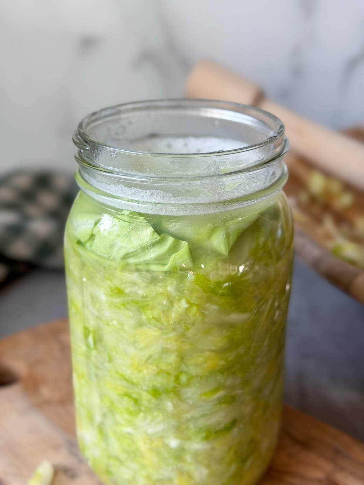 A quart mason jar full of cabbage and a few inches of brine, a large cabbage leaf is on top, keeping the finer cut cabbage pieces below.