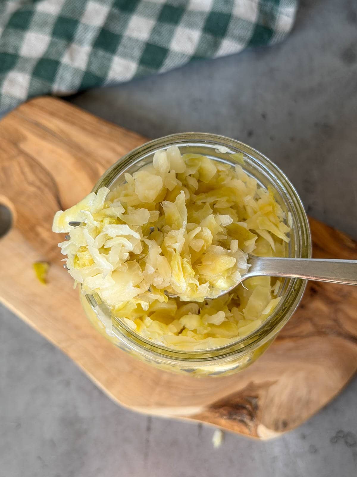 A quart mason jar is full of sauerkraut, a fork is inserted into the top portion of kraut, pulling some of it out of the jar as it's removed from the container.