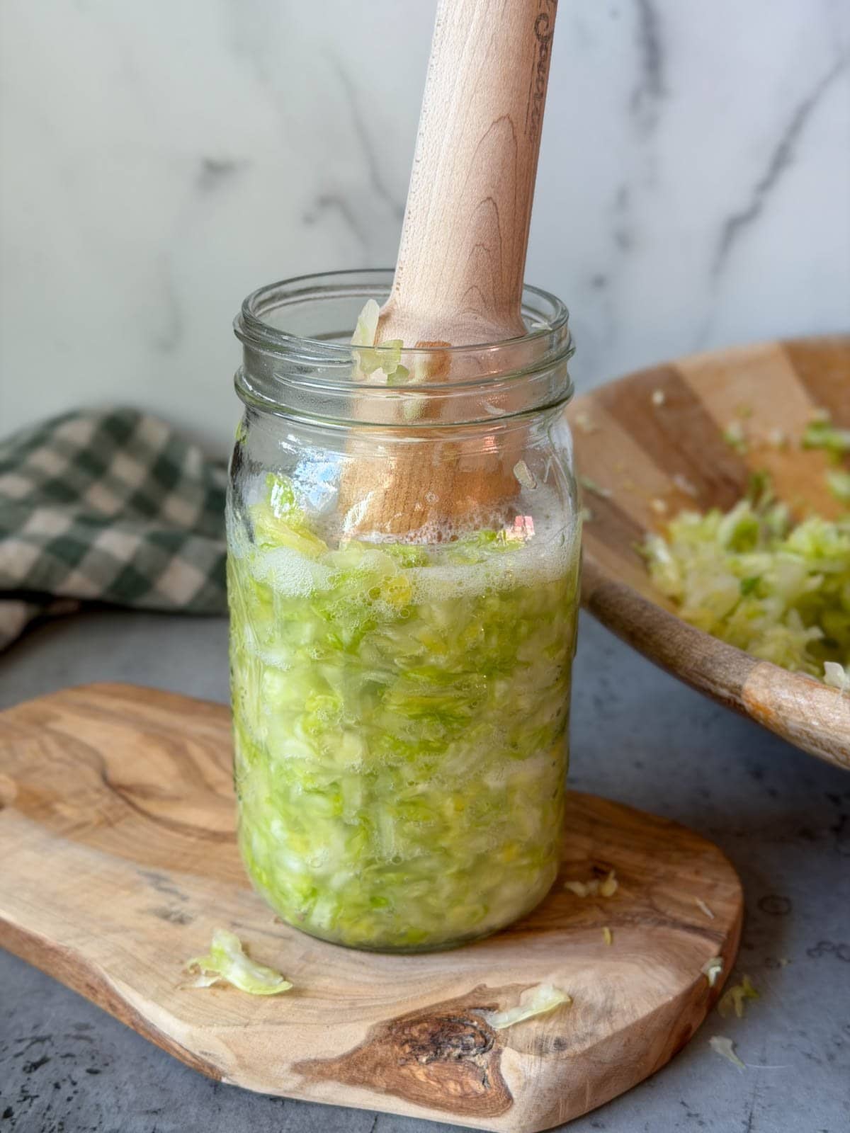 A wooden pounder is being used to press and pack cabbage into the jar.