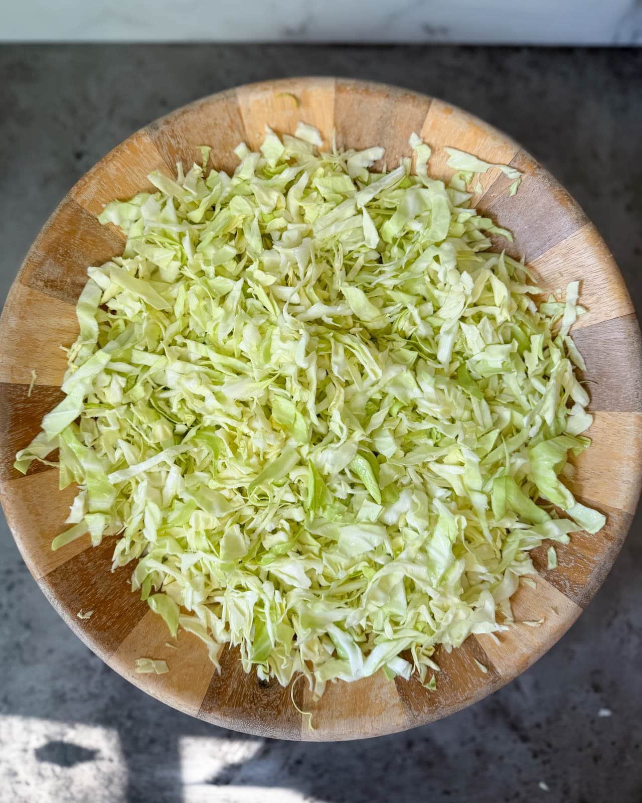 A large wooden bowl is full of shredded or cut cabbage for our sauerkraut recipe.