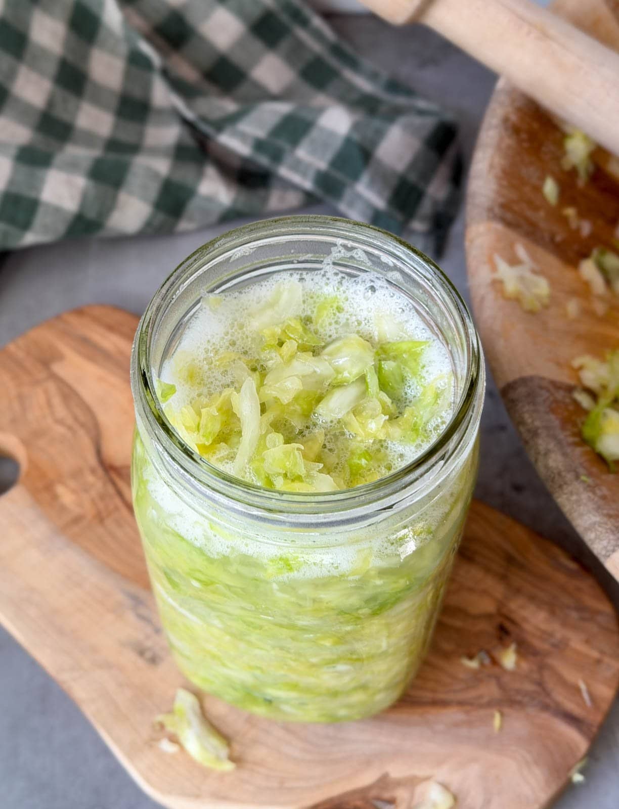 A quart jar is full of processed cabbage while a few bubbles have formed on top due to being packed tight with a pounder.
