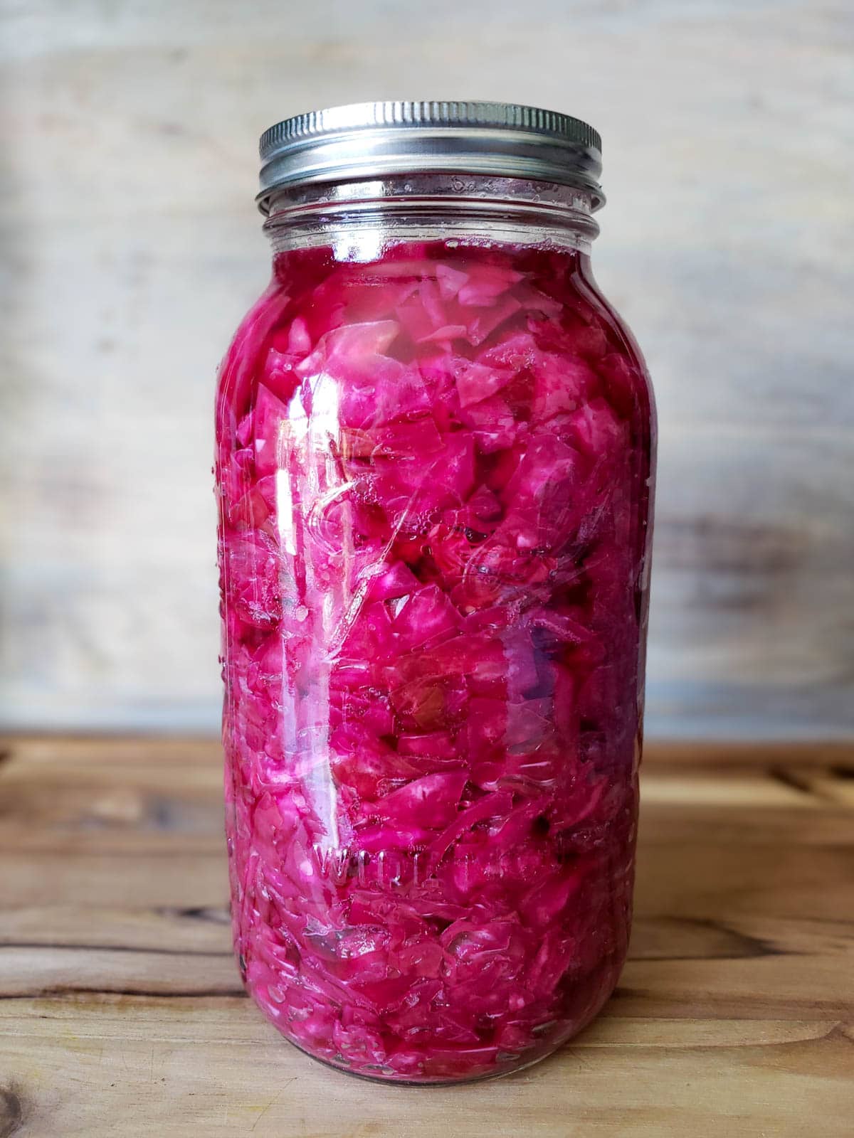 A large half gallon mason jar full of sauerkraut that has turned a pinkish purple in color due to using some red cabbage in the recipe.