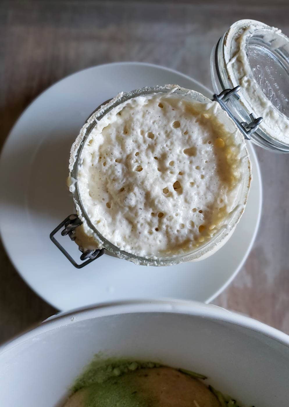 a close up of active sourdough starter in a jar, looking down on the jar with the lid open and the starter bubbly and risen to the top