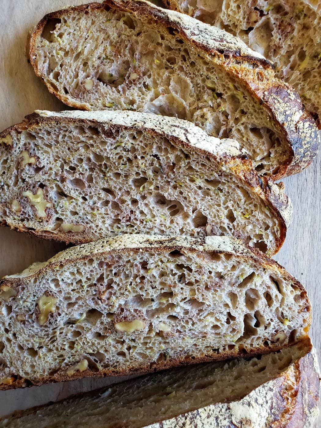 A close up of 3 slices of rustic sourdough zucchini bread, showing nice even air holes, walnut pieces, and some green specks of zucchini 