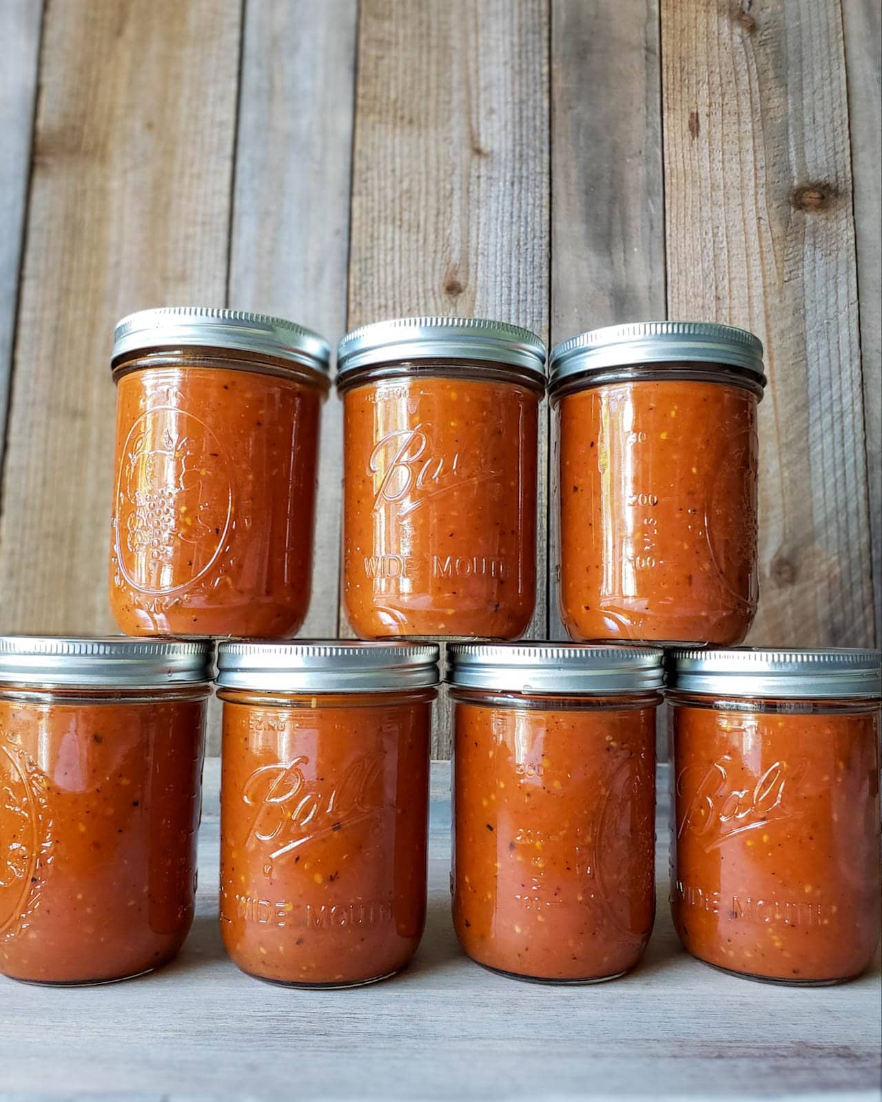 Two rows of pint mason jars stacked atop one another with four jars on the bottom and three jars on top full of roasted tomato sauce.