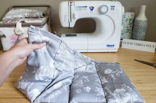 A rice heating pad is being held up by one end in front of a sewing machine.