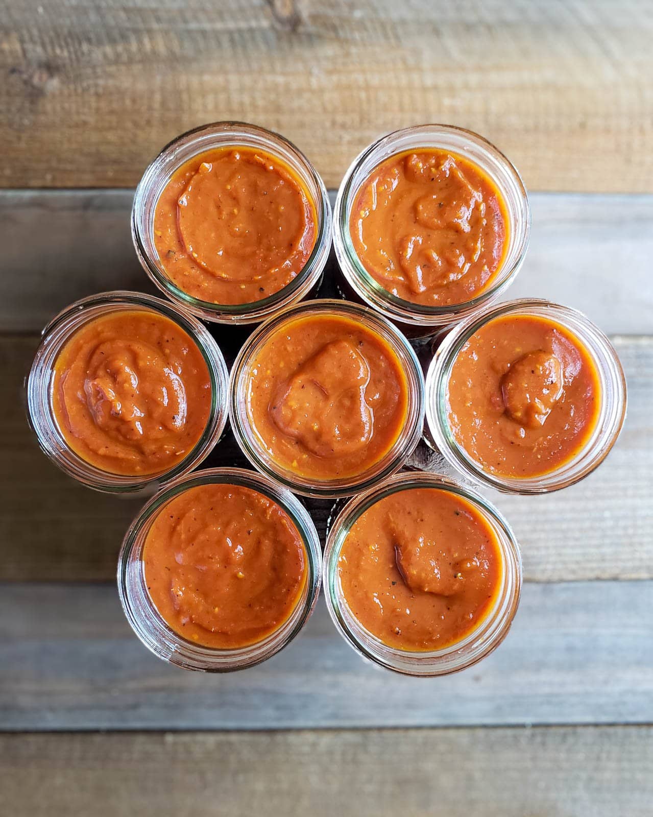 Three rows of jars with three in the middle and two in the top and bottom arranged in a honeycomb pattern are full of sauce.