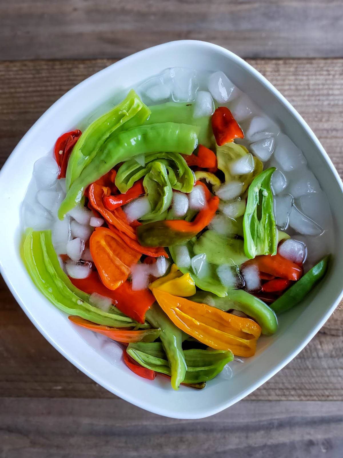 colorful chili peppers sitting in a white ceramic bowl filled with ice water. They are being rapidly cooled after blanching to help stop the cooking process.