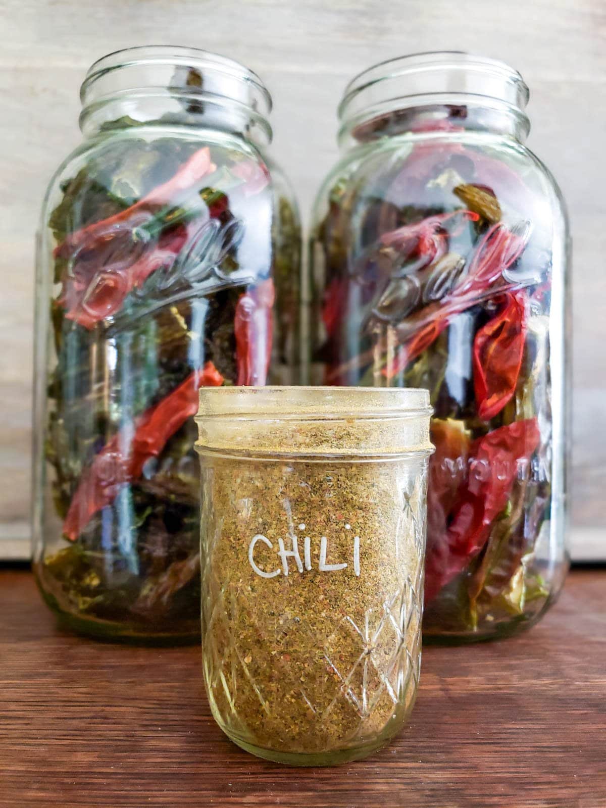 Two large half gallon mason jars full of dehydrated peppers along with a small jar of homemade chili powder in front. 