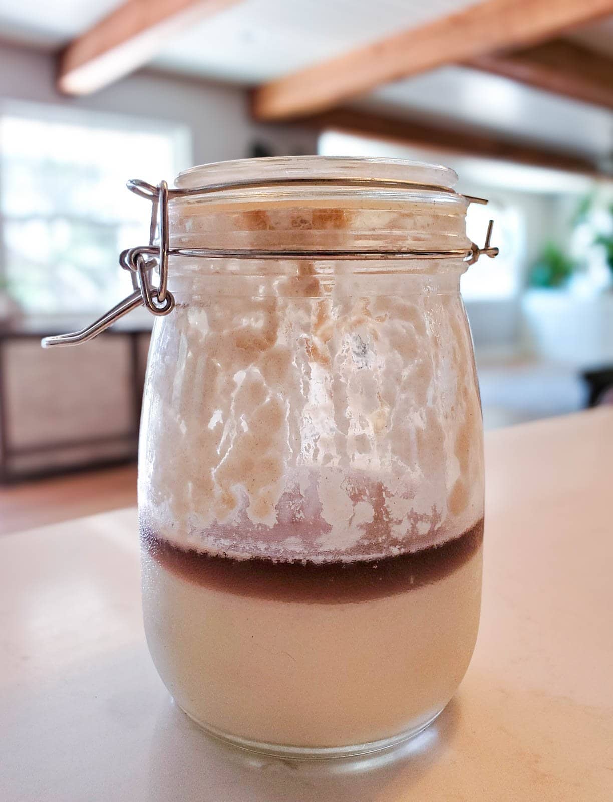 A flip top jar with a white starter on the bottom which is covered with a clear dark brown liquid on the top.