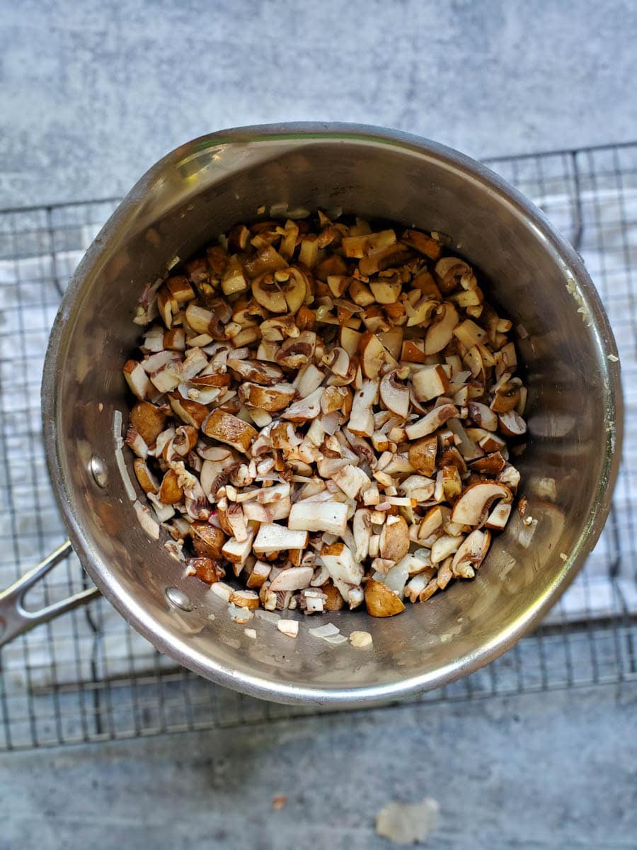 A close up inside a saucepan with finely chopped brown mushrooms added to the bottom of the pan along with the shallot and garlic.