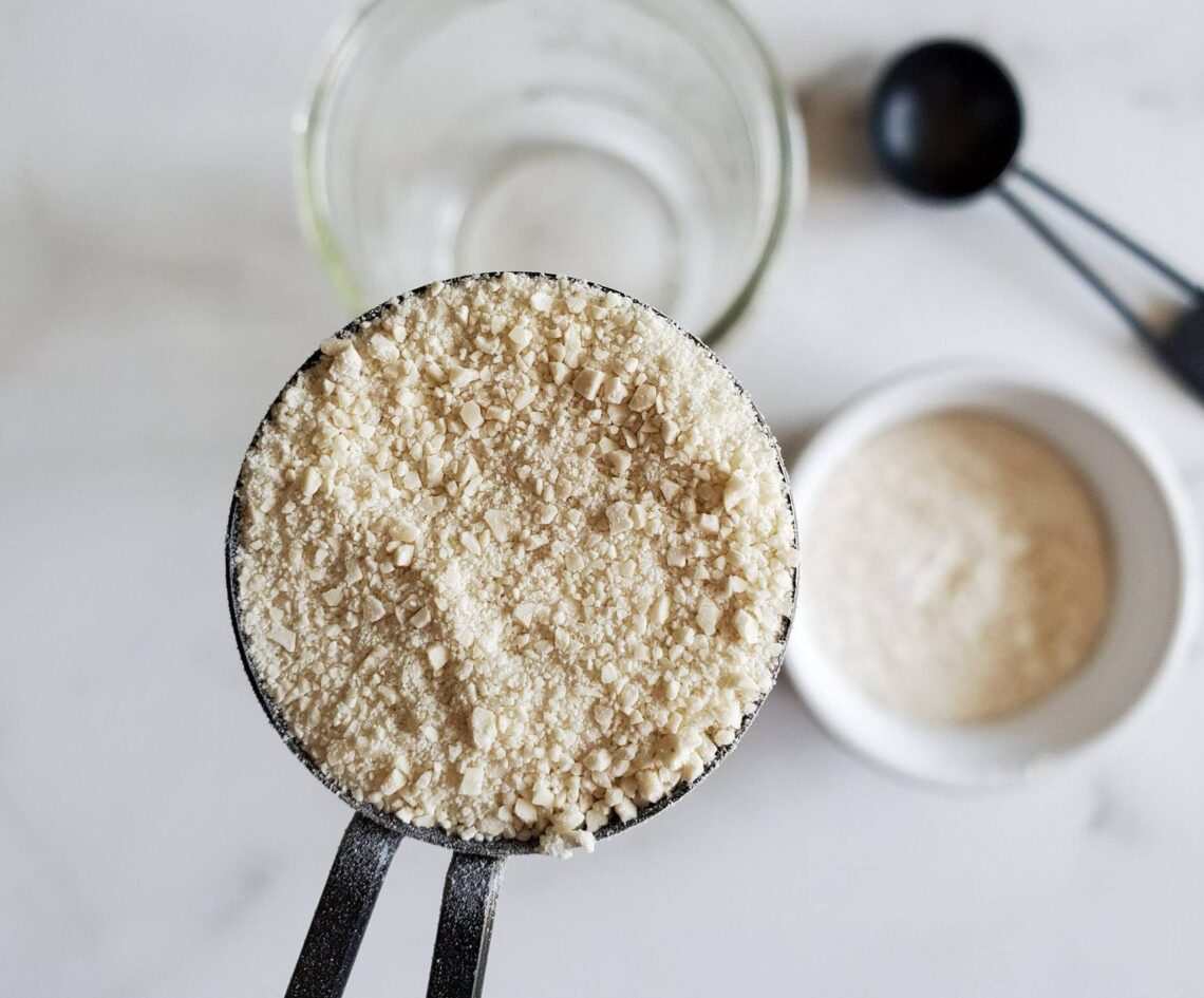 a close up of a tablespoon full of dry sourdough stater powder, with a jar of water and flour in the backgroun