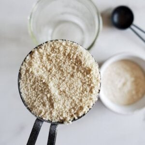 a close up of a tablespoon full of dry sourdough stater powder, with a jar of water and flour in the backgroun
