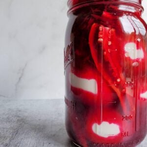 A large mason jar is full of bright red pickle beet brine and hardboiled eggs.