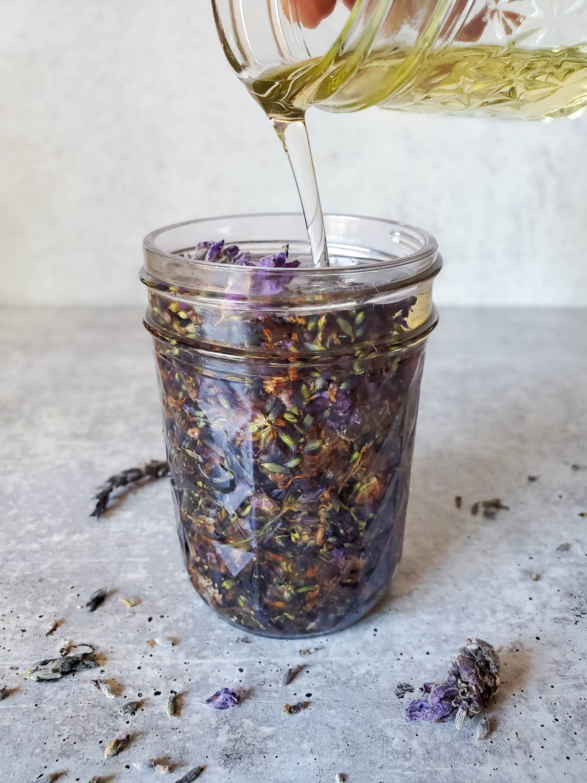 Oil is being poured into a jar of lavender flowers to infuse. 