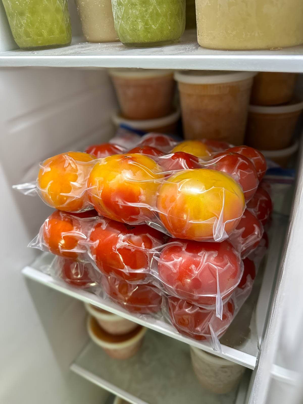 a neat stack of three ziplock bags full of red and yellow tomatoes inside a freezer