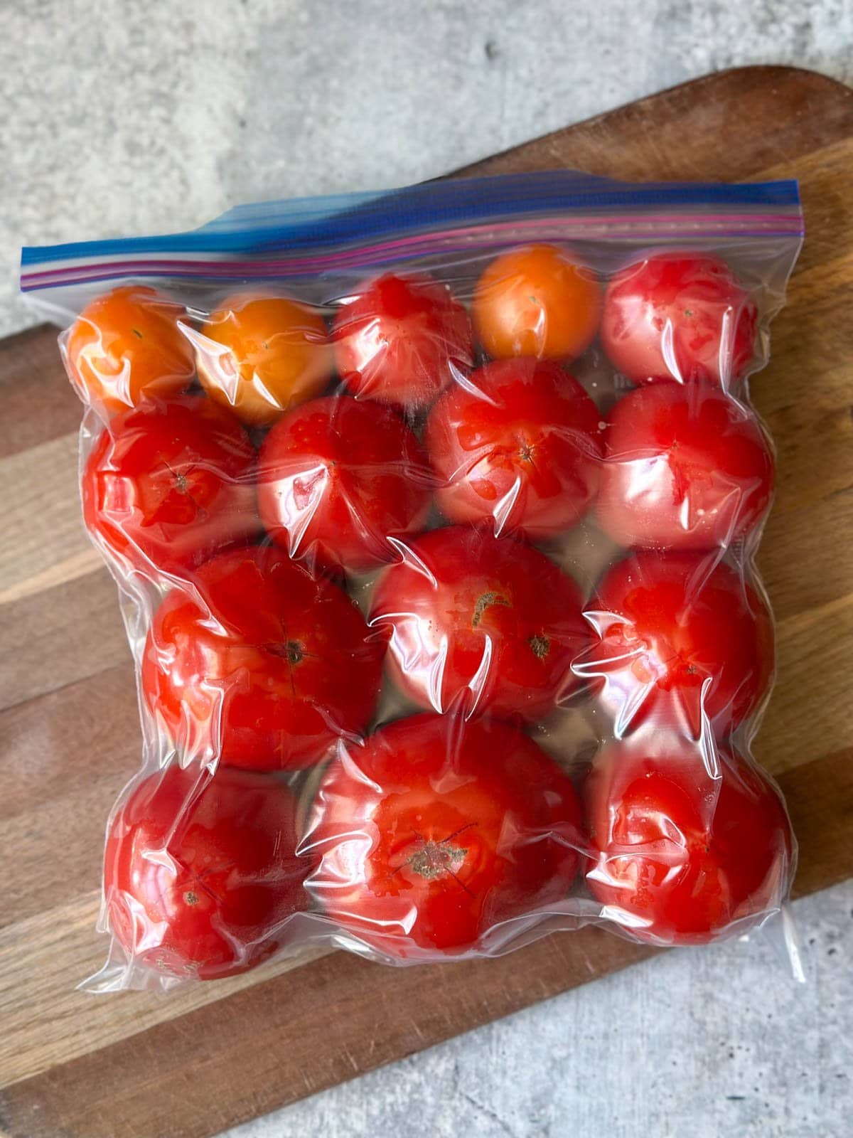 looking down on a ziplock bag full of about a dozen tomatoes, with the bag hugging the tomatoes and the air sucked out of it similar to a vacuum seal