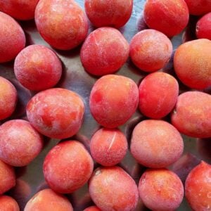 Many frozen red tomatoes arranged in a single layer.