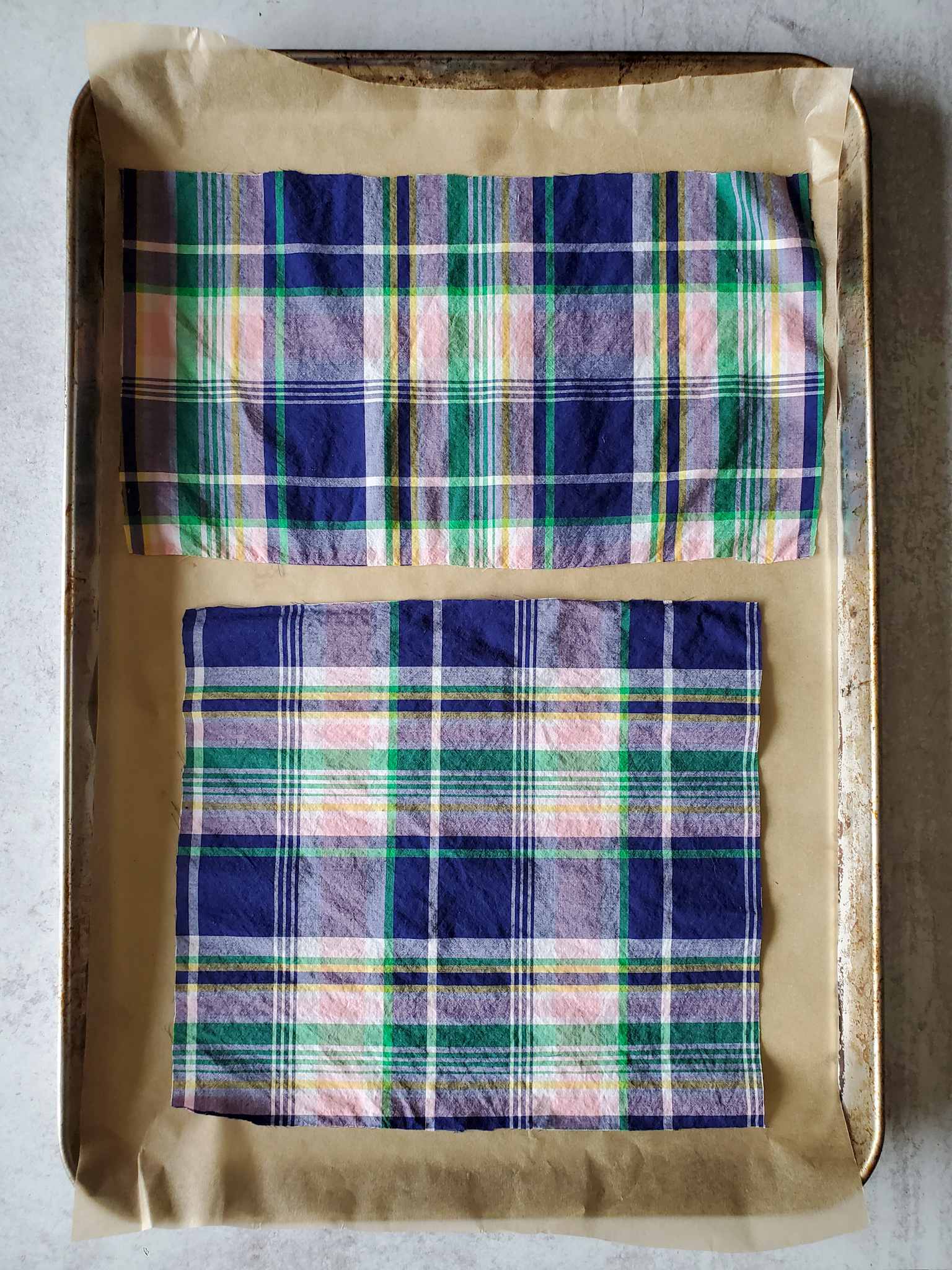 Two pieces of plaid cotton fabric are laid out on a baking sheet lined with parchment paper.