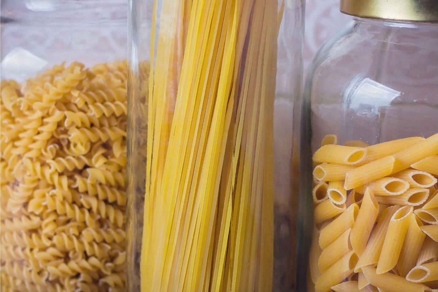 A few varieties of dried pasta in large glass storage containers.