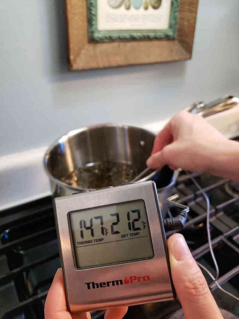 A temperature is being taken with a digital probe thermometer of cannabis coconut oil while it infuses. The temperature reads 147 degrees Fahrenheit.