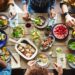 A dining table is full of a number of different food dishes in various serving dishes and there are people seated surrounding the table.