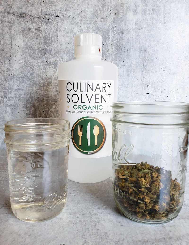 A half pint mason jar is on the left filled with ethyl alcohol, to the right is a pint mason jar with 8 grams of decarbed cannabis in it, behind and in between the two mason jars is a quart bottle of 200 proof ethyl alcohol.