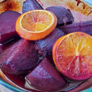 A glass baking dish full of roasted beets with two orange slices on top.
