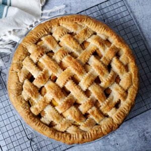 A pie with a latticed sourdough pie crust is cooling on a wire rack.