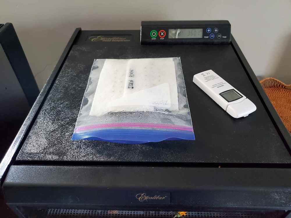 An Excalibur dehydrator with a Ziploc bag on top with moist paper towels inside that have been folded up, each one containing a different seed from a different year.