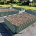 Metal raised beds filled with soil and their drip irrigation lines hooked up on top of the soil, lined up in equally spaced rows.