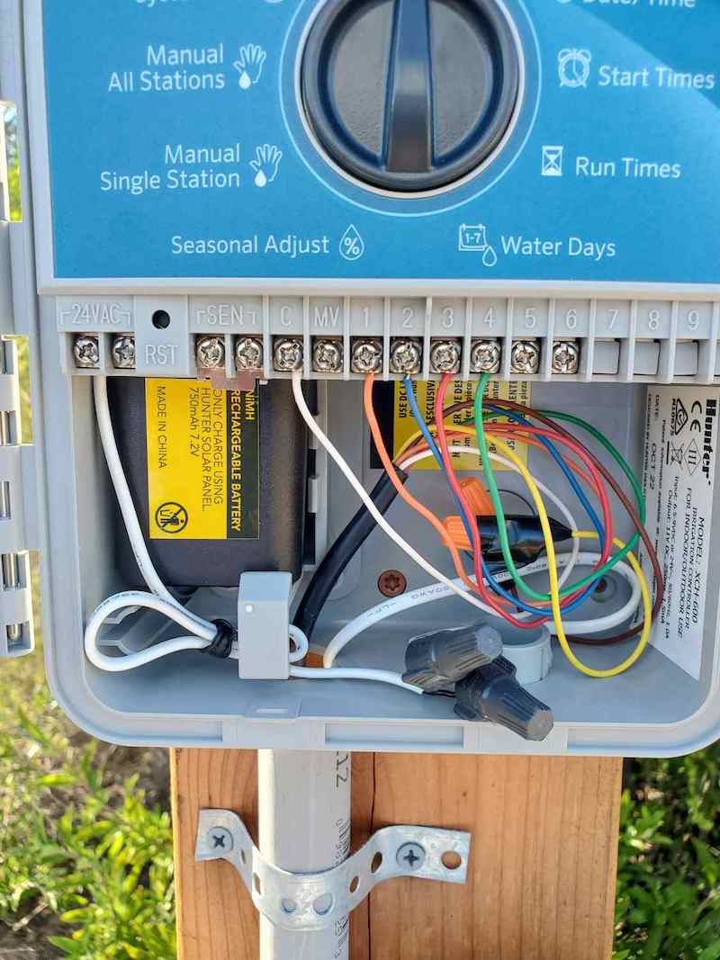 The inside wiring of the irrigation controller is shown. A variety of colored wires are connected to each of the zones and control. 