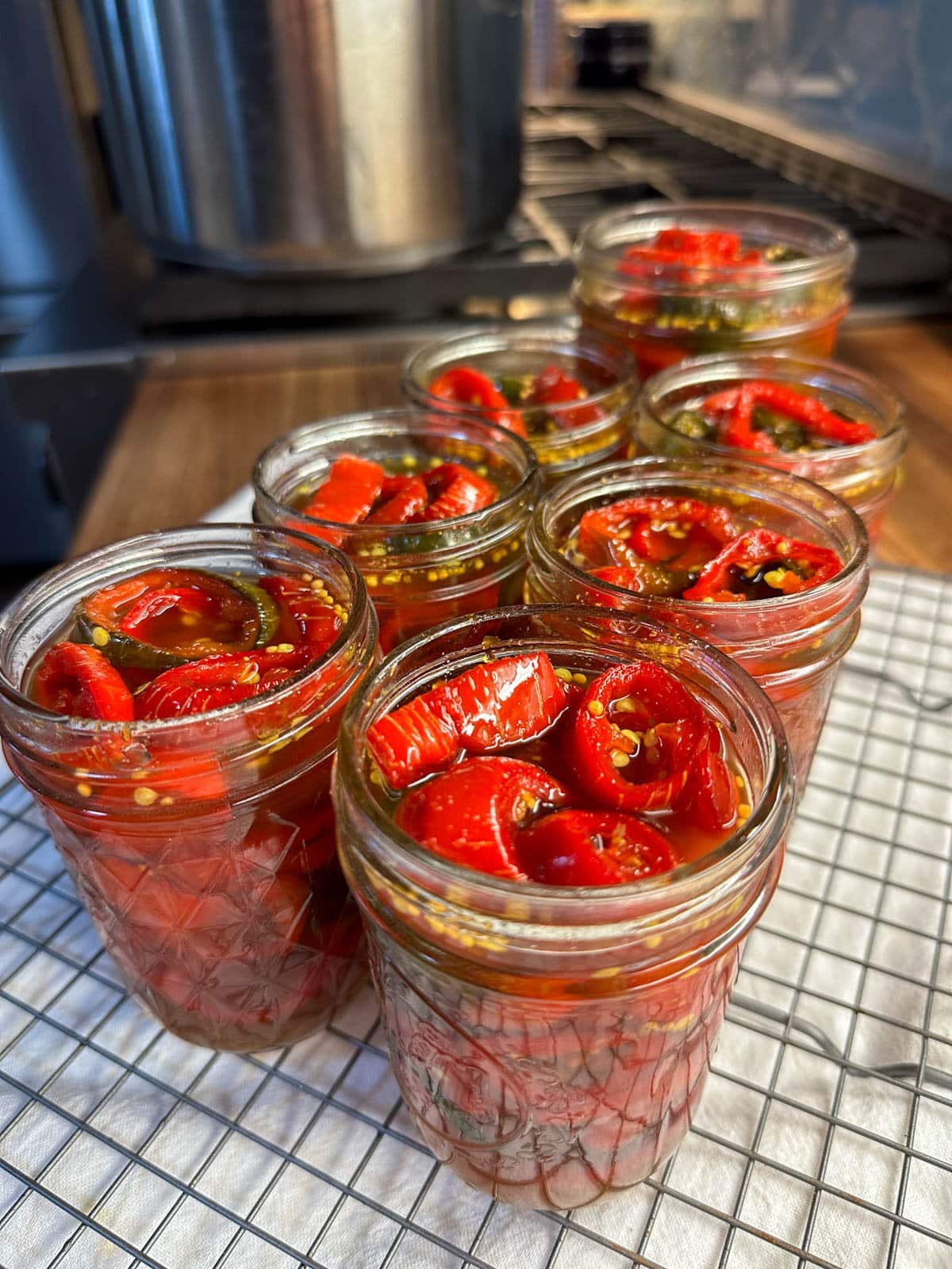 A close up of 7 canning jars full of bright red cowboy candy jalapeno rings, rather than the usual green color