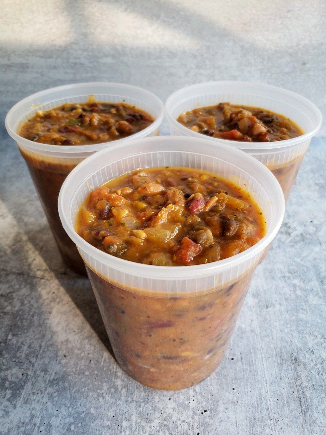 Three plastic quart containers full of chunky pumpkin chili, without lids and arranged in a triangle with a simple grey background