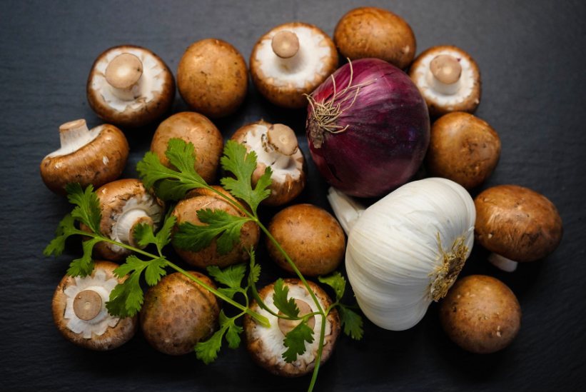 An overhead flatlay of the ingredients used to make vegan mushroom gravy, including garlic, red onion (shallot) and various mushrooms.